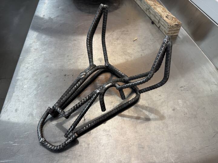 A horse head sculpture built from bent and welded rebar, resting on a steel workbench.